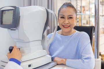 Fototapeta na wymiar Middle aged asian woman examining eyesight modern machine equipment by an eye specialist in clinic. Eye health examination concept.