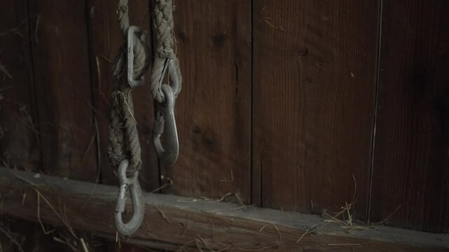 Farm slip or lifting hooks on rope against a wooden wall, medium shot