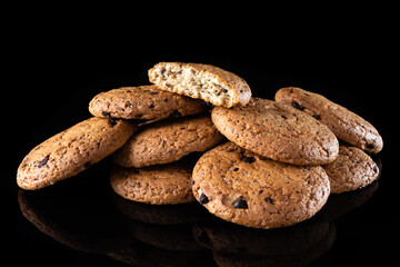 Oatmeal cookies with chocolate chips are isolated on a black background with a reflection. Lots of brown round homemade cookies lying on a reflective surface, close-up