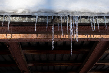 Long icicles hang from the snow-covered roof. Icicles falling danger concept.