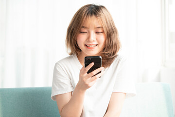 Young asian girl sitting on the sofa using the phone with a cheerful face