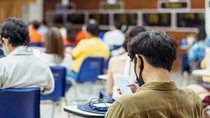 Back view of Asian man wear protective face mask to prevent Coronavirus(COVID-19) sitting on a chair for social distancing in  auditorium. Conference concept in coronavirus pandemic.Selective focus.