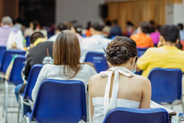 Back view of Asian woman wear protective face mask to prevent Coronavirus(COVID-19) sitting on a chair for social distancing in  auditorium.Conference concept in coronavirus pandemic.Selective focus.