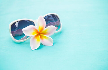 Summer concept background, beautiful fresh Plumeria flower with sunglasses with space on blue background, beauty and fashion concept