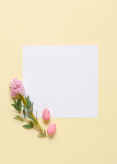 White invitation card mockup with eucalyptus branches, pink hyacinth and eggs on a yellow background.