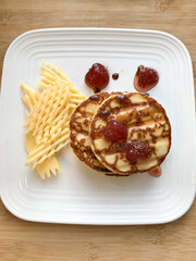 Beautiful homemade pancakes with strawberry and raspberry red jam on a white brick wall background.