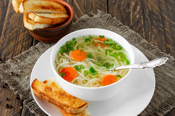 Chicken bouillon with noodles and carrot slices on a wooden table in rustic style