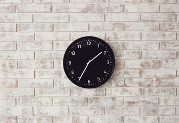 Stylish clock hanging on brick wall