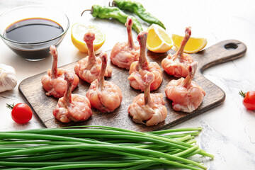 Board with raw chicken lollipops on light background