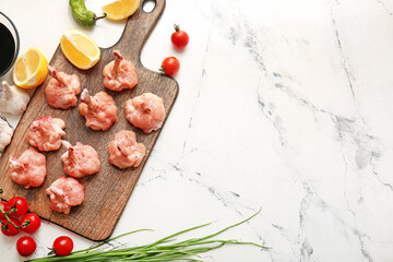 Board with raw chicken lollipops on light background