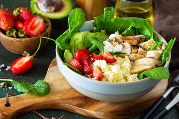 Healthy food, diet lunch menu concept, ketogenic diet and paleo diet. Couscous salad with strawberries, grilled chicken, avocado and feta cheese on a stone table.