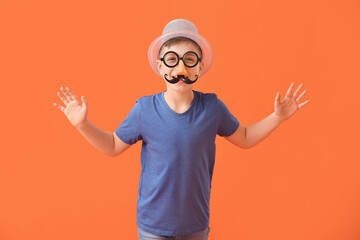 Little boy in funny disguise on color background. April Fools Day celebration