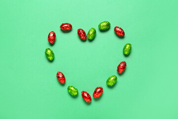 Heart made of sweet chocolate eggs on color background