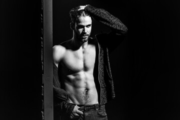 Sexy man with muscular bare torso in studio on black and brick wall background, copy space.
