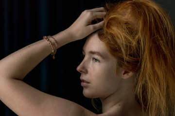 Face close up of Ginger hair young white model combing her hair upward with black background
