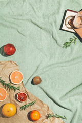 Summer scene with fruits,rosemary, glass of water and books on pastel green beach towel. Drinks and refreshment concept. Sunlit flat lay. Minimal style. Top view.