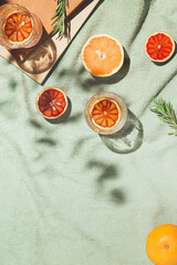 Summer scene with fruits,rosemary, glass of water and books on pastel green beach towel. Drinks and refreshment concept. Sunlit flat lay. Minimal style. Top view.