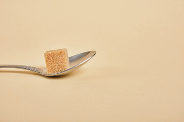 metal spoon with brown sugar cube on beige background, health care and diabetes concept