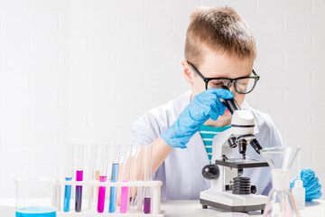 A schoolboy with a microscope examines chemicals in test tubes, conducts experiments - a portrait on a white background. Concept for the study of coronavirus in the laboratory