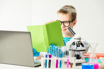 A schoolboy with a microscope and book examines chemicals in test tubes, conducts experiments - a portrait on a white background. Concept for the study of coronavirus in the laboratory