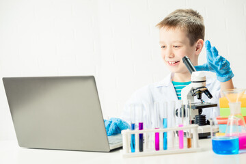 Schoolboy with a laptop in the laboratory conducts chemical experiments with substances in test tubes, portrait of a young chemist