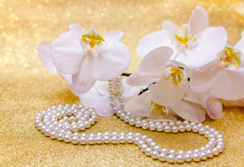 Obraz na płótnie Canvas white Orchid and pearl necklace on a shiny gold background 