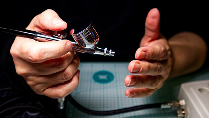 Female hand holding an airbrush isolated on dark background. Selective focus