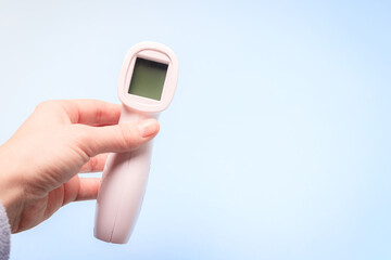 infrared thermometer on a blue background in your hand. the thermometer in his hand . prevention. non-contact temperature measurement. health. coronavirus. pandemic. human health. check the temperatur