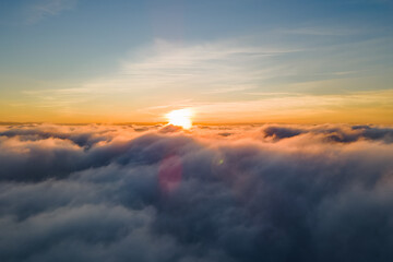 Aerial view of bright yellow sunset over white dense clouds with blue sky overhead.