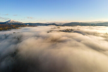 Aerial view of a small distant village houses on hill top in fall foggy mountains at sunrise.