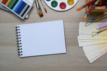 Top view of Artist workspace on wooden background with sketchbook, watercolor, brushes pencils and crayons. Drawing class education.