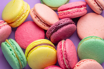Colorful sweet macarons or macaroons, flavored cookies on purple background.