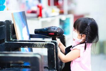 Naklejka premium Pupil child are using a dryer to their own watercolor artwork to dry the paint. Cute girl wearing a white cloth mask. Art class on canvas in indoors. Side view of a 3-4 year old kids.