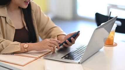 Young woman sitting in cafe using mobile phone and working with computer laptop.