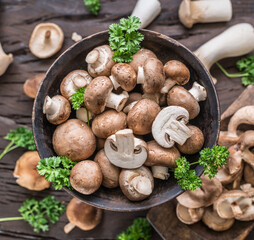 Different brown colored edible mushrooms on wooden table with herbs. Top view.