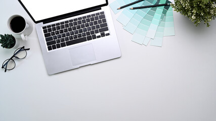 Top view of graphic designer workplace with computer laptop, color swatches, plant and copy space on white background.