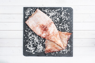 Raw squid carcass with spices and coarse salt on a black slate board. copy space Top view.