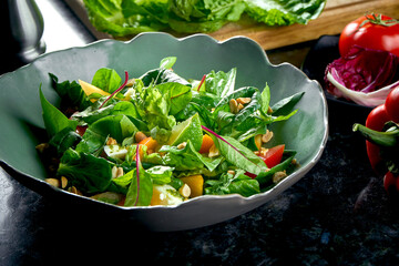 Mix salad with persimmon, mozzarella, spinach and nuts, served in a green bowl on a dark marble background. Veggie salad. Restaurant food