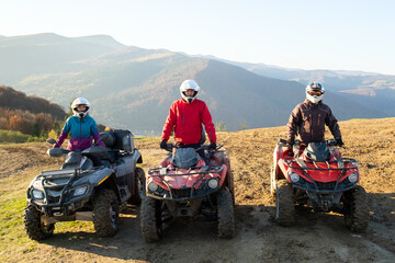 Happy drivers in protective helmets enjoying extreme riding on ATV quad motorbikes in summer mountains at sunset. © bilanol