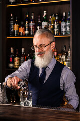 Barman making a cocktail and putting a large ice cube into the glass on the bar counter