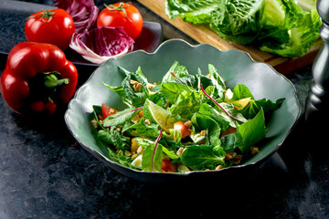 Mix salad with persimmon, mozzarella, spinach and nuts, served in a green bowl on a dark marble background. Veggie salad. Restaurant food