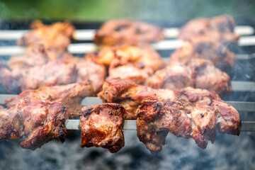 Shashlik or shish kebab preparing on barbecue grill over hot charcoal. Grilled pieces of pork meat on metal skewers.