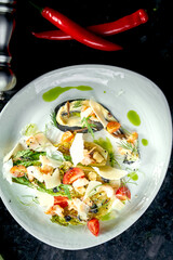 Mixed salad with grilled shrimp, parmesan and artichoke served in a white plate on a dark marble background. Restaurant food.