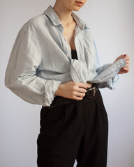 Woman wearing stylish outfit with oversized shirt and black trousers isolated on light background