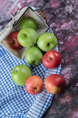Red and green apples out of a basket on the checked towel