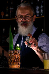 Stylish brutal barman makes a cocktail at bar counter background