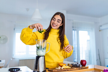 Young woman making detox smoothie at home. Girl making smoothie of fruit and vegetables. Healthy...