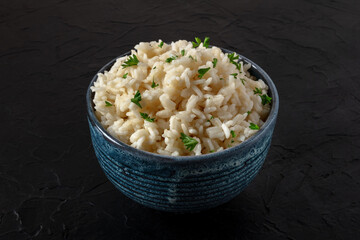 White rice with parsley leaves in a blue bowl, on a dark black background