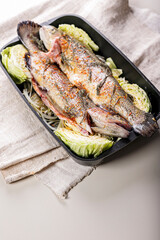 Fresh trout with spices and vegetables. Freshwater fish with saffron, red onion and cabbage in a cast iron baking dish. Light background. Vertical shot
