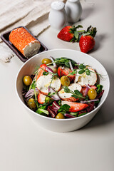 Delicious salad with fresh strawberries, red onions, ice salad, goat cheese and olives. Food still life on a light background. Organic farm products. Healthy food. Vertical shot. Copy space